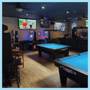Inside of Leo's Lair, we see an aged word floor with several pool tables. Against the far wall are several Video Lottery machines. On the walls are several TVs playing local sports.