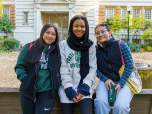 Three college women pose in front of a campus building