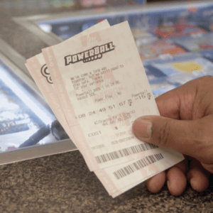 closeup of a hand holding a Powerball and Megabucks ticket over a check-out counter