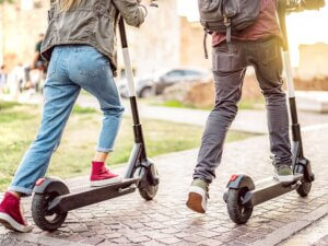 Two school-aged kids viewed from behind as they ride scooters.