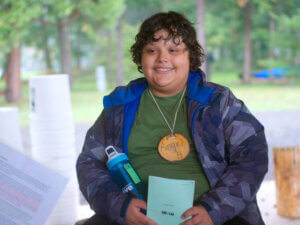 A boy with a "wood cookie" name tag holds a water bottle and smiles.