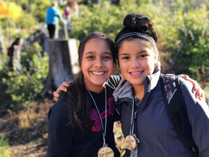 Two campers posed with their arm around the other's shoulders smile at the camera