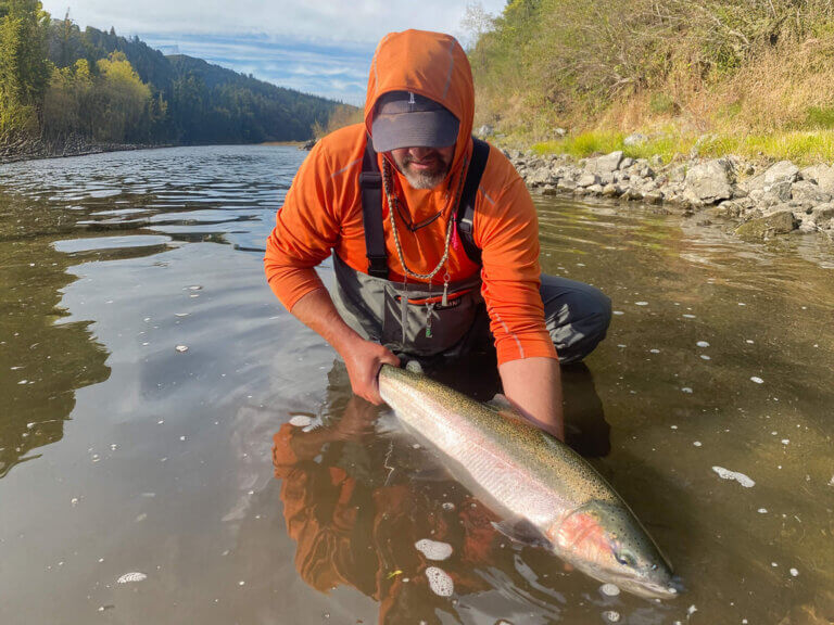 A man in waders grasps a large fish as he removes it from the water